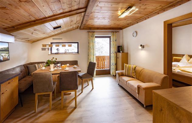 Ein gemütliches, modernes Wohnzimmer mit Holzdecken und einem Esstisch. Der Raum verfügt über eine Ecke zum Entspannen und einen Balkon mit Blick nach draußen.