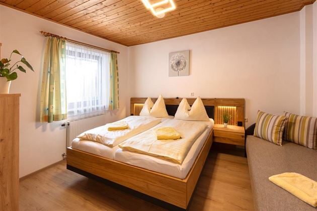 Ein gemütliches Schlafzimmer mit einem großen Doppelbett und einer Aussicht auf das Fenster. Die Wände sind hell, und eine Couch ist für zusätzlichen Komfort vorhanden.