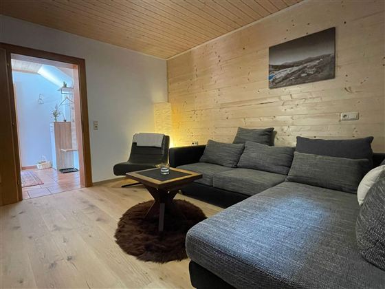 Ein modernes Wohnzimmer mit einer gemütlichen Couch und einem kleinen Tisch. An den Wänden sind Holzverkleidungen und das Licht sorgt für eine angenehme Atmosphäre.