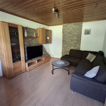A cozy living space with a brown couch and a coffee table. On the wall, there is a television and a wooden display cabinet.