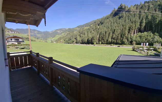 A beautiful balcony overlooking a green meadow and wooded hills. The clear sky is a perfect complement to the idyllic landscape.