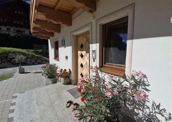 An inviting entrance with a wooden door and beautiful flower boxes. The sun is shining, and the surroundings are well-maintained and friendly.