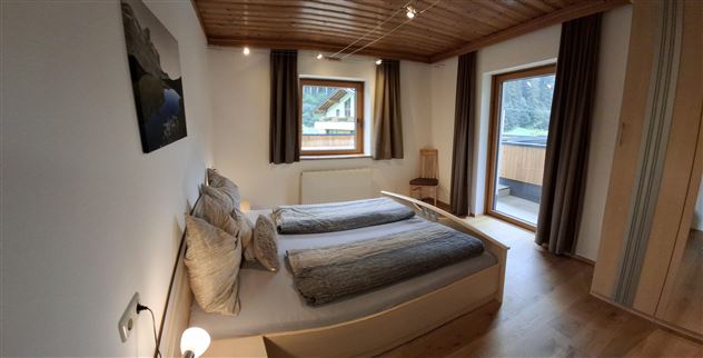 A modern bedroom with two single beds and bright wooden elements. Large windows let in plenty of natural light and offer a view outside.