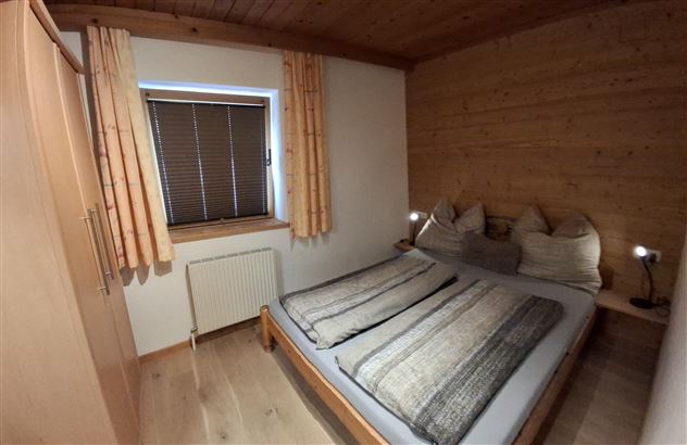 A cozy bedroom with a double bed and wood paneling. Large windows with curtains let in plenty of light.