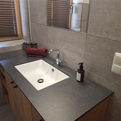 A modern bathroom with an elegant sink and wooden base. On the surface are a soap dispenser and a towel.