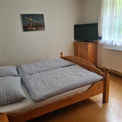 A simple bedroom with a double bed and two pillows.  
A picture is hanging on the wall, and a television is standing on a wooden cabinet.