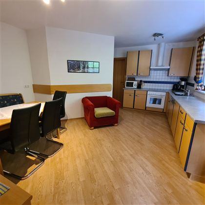 A cozy kitchen with a dining area and a red armchair. The furniture is modern and the room feels inviting.