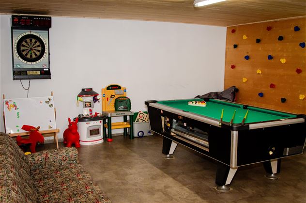A room with a billiard table and a dartboard on the wall. There are also toys and a climbing wall.