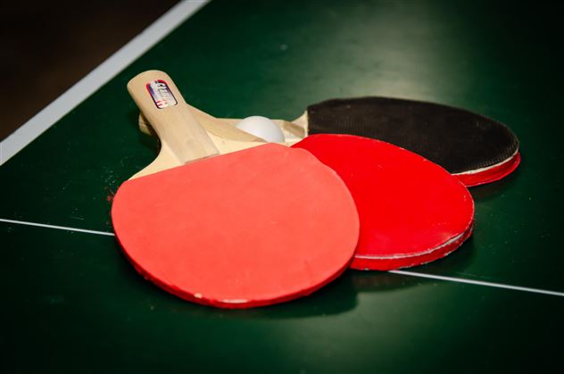 Three table tennis paddles are lying on a green table tennis field. Two paddles are red and one is black.