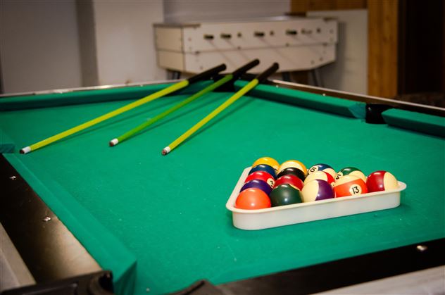 A billiard table with green felt and three cue sticks. A bowl of colorful billiard balls is on the table.