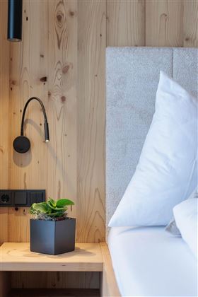 Ein stilvolles Schlafzimmer mit einem gemütlichen Bett und einer Holzverkleidung. Auf dem Nachttisch steht ein kleiner Blumentopf mit einer grünen Pflanze.