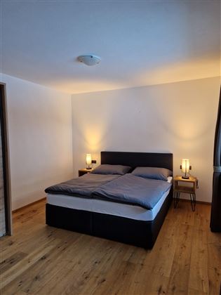 A modern furnished bedroom with a double bed and nightstands. The walls are light and the lighting creates a cozy atmosphere.
