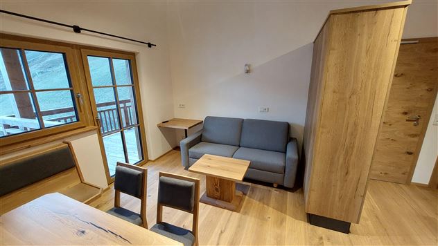 A cozy living area with a gray sofa and a wooden table. Large windows provide a beautiful view outside.