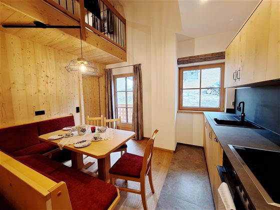 A cozy kitchen with a wooden dining table and chairs. The walls are made of light wood, and there are large windows that provide plenty of light.