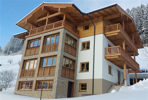 Ein modernes chaletartiges Haus in den Bergen. Es ist mit Holzverkleidung und großen Fenstern gestaltet und von Schnee umgeben.