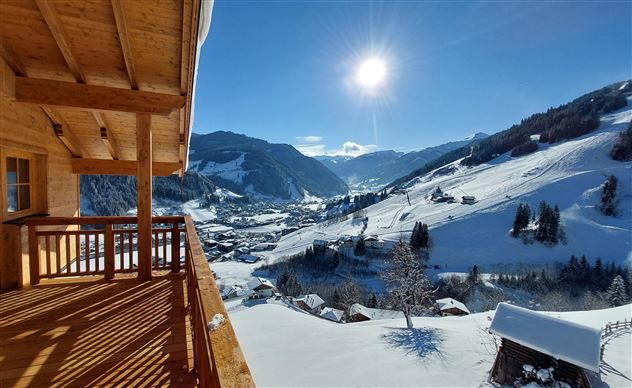 Eine verschneite Landschaft mit Bergen und einem klaren blauen Himmel. Die Sonne scheint über einem malerischen Tal und freundlichen Hütten.