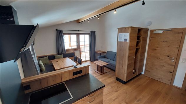 Eine moderne Wohnküche mit holzverkleideten Wänden und einer gemütlichen Sitzecke. Große Fenster lassen viel Licht herein und bieten einen Blick nach draußen.