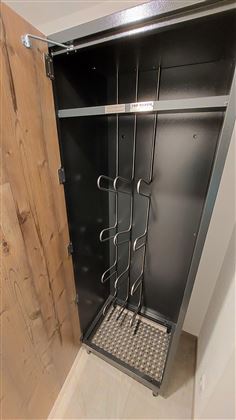 Ein offener, moderner Schrank mit einer metallenen Innenseite und mehreren Haken. Der Boden ist mit einer rutschfesten Matte ausgelegt.