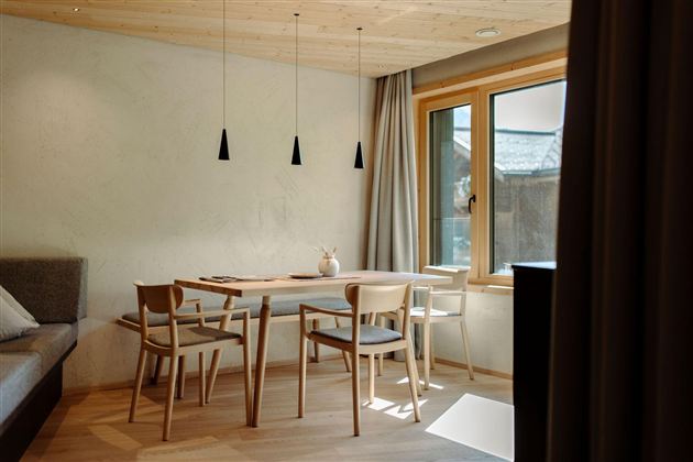 A modern furnished room with a wooden table and chairs. Large windows bring in plenty of daylight into the room.