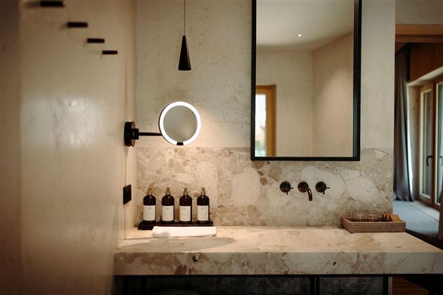 An elegant bathroom with a marble washbasin and modern fittings. In the background, there is a mirror with a lighted frame.