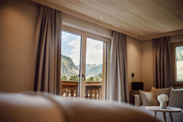 A cozy room with large windows and a view of the mountains. The decor is modern and bright, with soft colors.