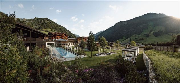 A picturesque landscape with a swimming pool and modern buildings. Gentle hills and a clear sky frame the scene.