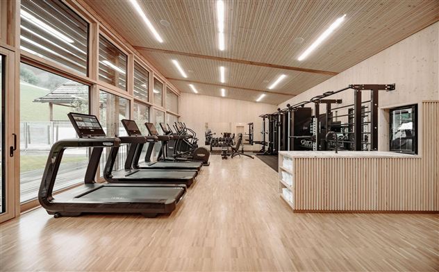 A modern gym with large windows and wooden paneling. Treadmills and exercise equipment are clearly visible.