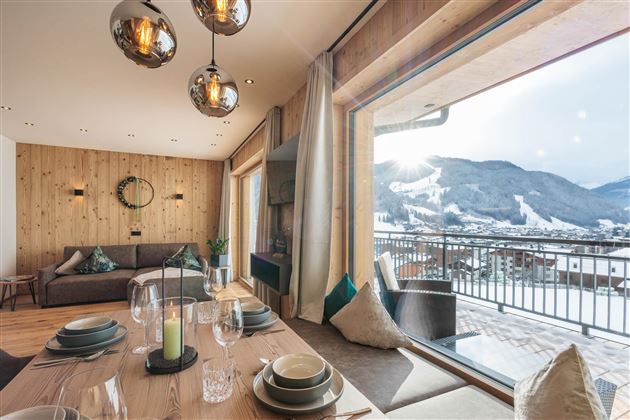 Ein modernes Wohnzimmer mit einer großen Fensterfront und Blick auf die Berge. Der Raum ist hell und freundlich, mit einer einladenden Essgruppe.