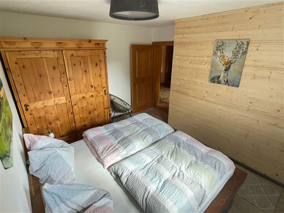 Ein gemütliches Schlafzimmer mit einem Doppelbett, bunten Bettdecken und einem Holzschrank. An der Wand hängt ein Kunstwerk eines Tieres.