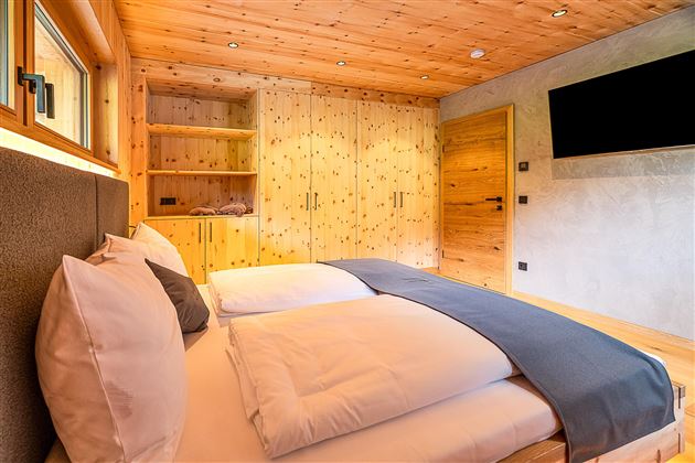 Ein gemütliches Schlafzimmer mit Holzverkleidung und einem großen Doppelbett. Die Wände sind hell und es gibt ausreichend Stauraum in Schränken.