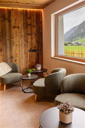 Ein modernes Wohnzimmer mit bequemen, grünen Sesseln und einem kleinen Tisch. Durch das Fenster ist eine grüne Landschaft mit Bergen im Hintergrund sichtbar.
