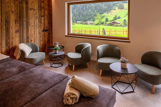 Ein modernes Wohnzimmer mit komfortablen Sesseln und einem großen Fenster. Durch das Fenster ist die grüne Landschaft der Alpen sichtbar.