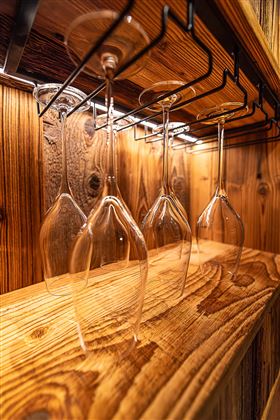 Eine Reihe von schlichten Weingläsern hängt an einem Holzregal. Der Hintergrund besteht aus warmem, rustikalem Holz.