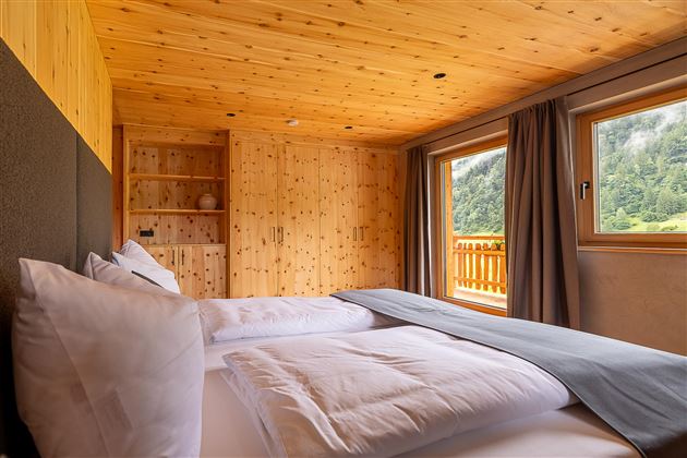 Ein gemütliches Schlafzimmer mit Holzverkleidung und großen Fenstern. Die Aussicht auf die Natur sorgt für eine entspannende Atmosphäre.