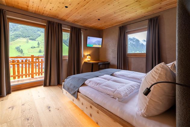 Ein gemütliches Schlafzimmer mit Holzwänden und großen Fenstern. Der Blick zeigt eine grüne Landschaft und eine moderne Einrichtung.
