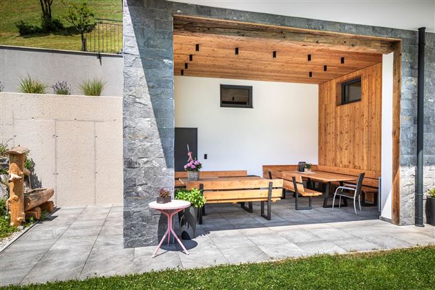 Ein gemütlicher Außenbereich mit Holzmöbeln und einem modernen, offenen Design. Die Terrasse ist von geräumigen Wänden aus Stein umgeben und lädt zum Entspannen ein.