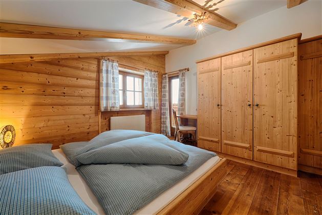 Ein gemütliches Schlafzimmer mit Holzverkleidung und einem Doppelbett. Der Raum ist hell und einladend, mit einem großen Kleiderschrank und einem Fenster.