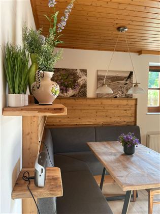Ein gemütlicher Essbereich mit einer Holzdecke und einer modernen Einrichtung. Auf dem Tisch stehen kleine Pflanzen, und die Wände sind mit Bildern dekoriert.