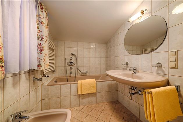 A modern bathroom with a bathtub and a sink. Yellow towels and a window with curtains create an inviting atmosphere.