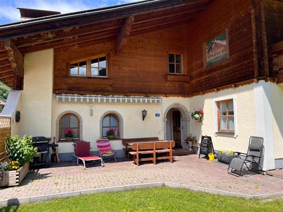 A cozy house with wooden cladding and a beautiful outdoor area. The terrace is decorated with chairs, a table, and plants.