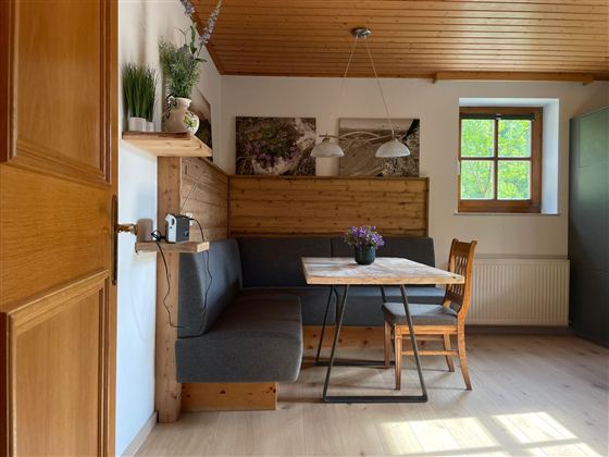 Ein gemütlicher Essbereich mit einer Couch und einem Tisch. Die Wände sind mit Holz verkleidet, und ein Fenster sorgt für natürliches Licht.