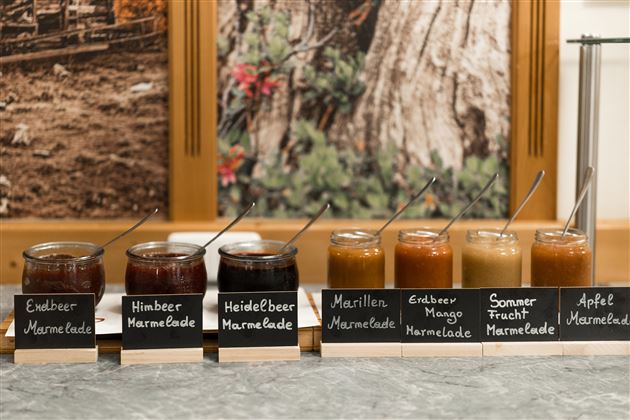 Eine Auswahl an Marmeladen in Gläsern auf einem Tisch. Die Sorten sind Erdbeer, Himbeer, Heidelbeer, Marille, Erdbeer-Mango, Sommerfrucht und Apfel.