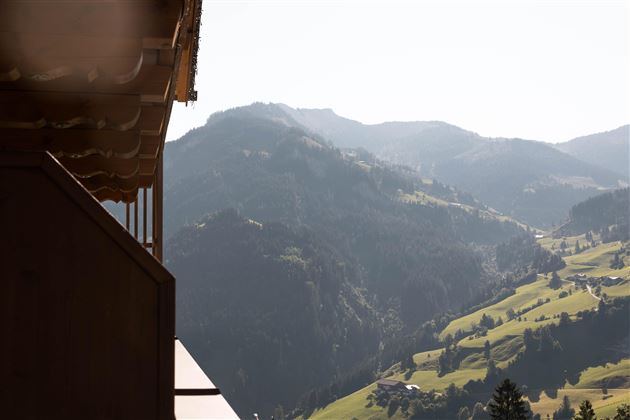 Eine Aussicht auf die Berge mit sanften Hängen und klaren Himmel. Im Vordergrund ist ein Teil eines Daches zu sehen.