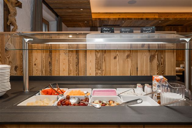 Ein Buffet mit frischem Obst und Joghurt in einer gemütlichen Umgebung. Die Holzverkleidung und die dekorativen Elemente verleihen dem Raum eine warme Atmosphäre.