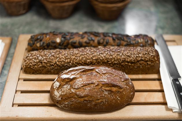 Drei verschiedene Brote auf einem Holzbrett. Zwei langgestreckte Brote und ein rundes Brot in der Mitte.