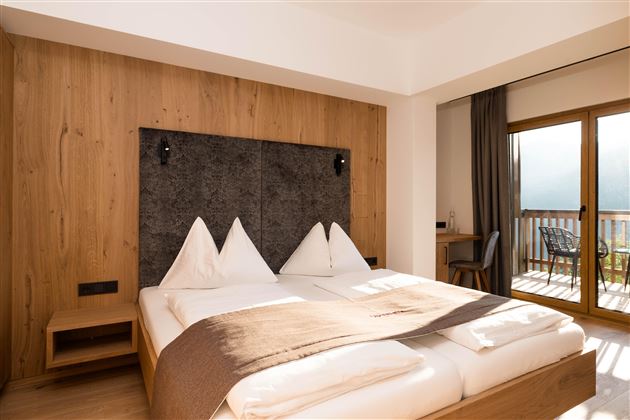Ein modernes Schlafzimmer mit einem großen Bett und Holzdekor. Der Raum verfügt über einen Balkon mit Aussicht.