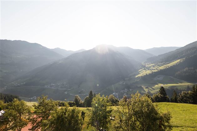 Eine malerische Berglandschaft bei Sonnenaufgang. Grüne Wiesen und Bäume umgeben die sanften Hügel.