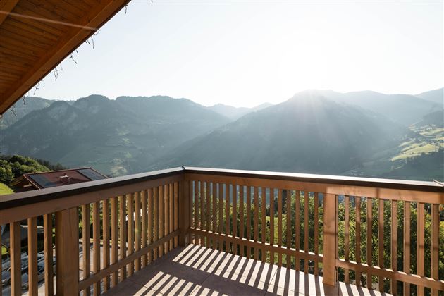 Eine sonnige Aussicht vom Balkon auf die Berge. Die Landschaft ist grün und hügelig, mit strahlendem Licht im Hintergrund.