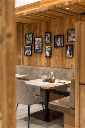 Ein gemütliches Restaurant mit Holzverkleidung und beigen Sitzen. An den Wänden hängen gerahmte Schwarz-Weiß-Fotos.