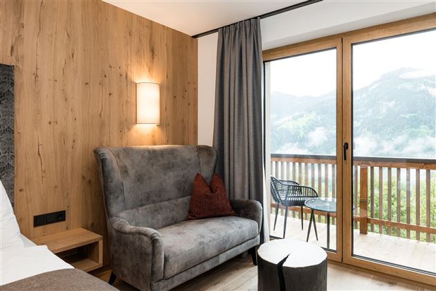 Eine gemütliche Sitzecke mit einem grauen Sessel und einem kleinen Tisch. Im Hintergrund sind große Fenster mit Blick auf die Berge.